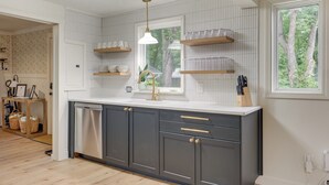 Een moderne keuken met donkergrijze kastjes, witte aanrechtbladen en een raam met uitzicht op bomen.