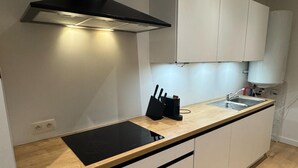 Una cocina moderna con una placa de inducción negra, un lavamanos de acero inoxidable y armarios blancos.
