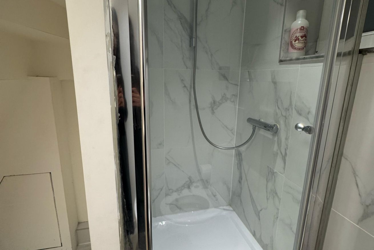 Ducha con paredes de vidrio, un cabezal de ducha manual y una botella de champú en un estante.
