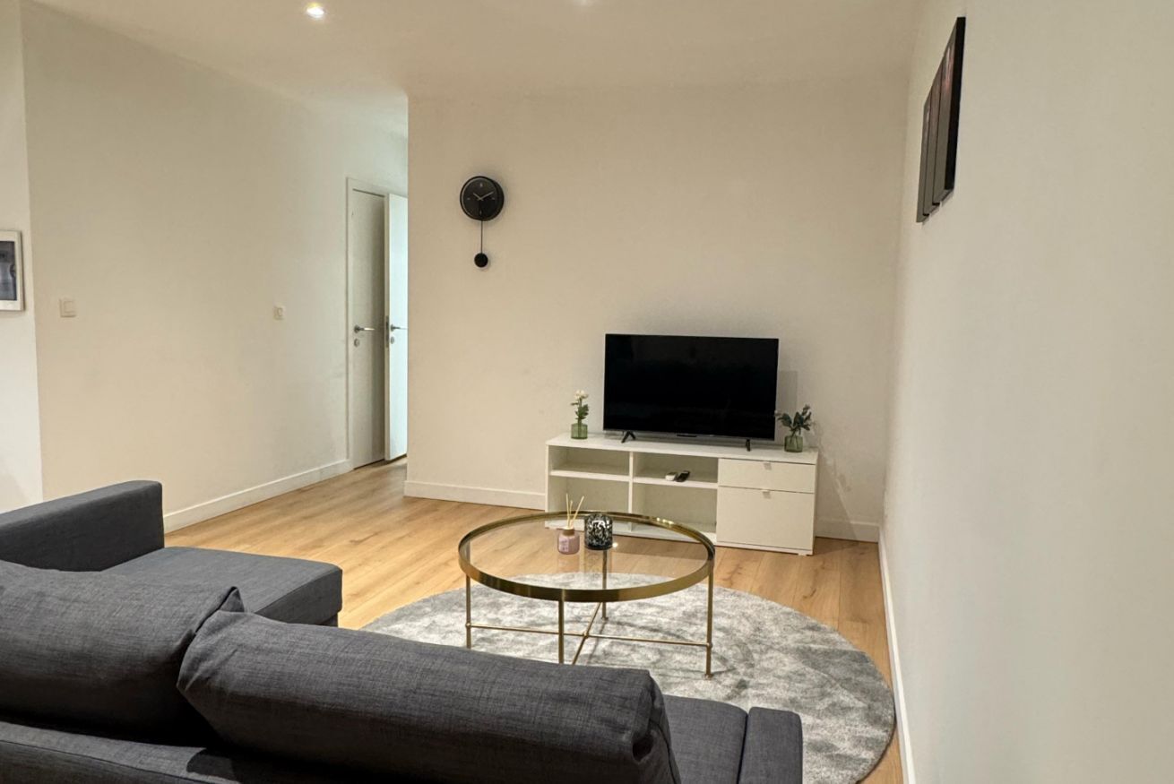 Un salon moderne avec un téléviseur à écran plat, une table basse en verre et un canapé gris.