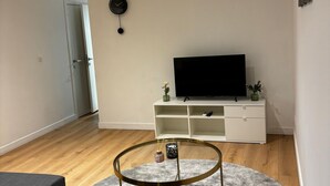 Una sala de estar con televisor, un mueble blanco, una mesa de centro redonda y un reloj en la pared.