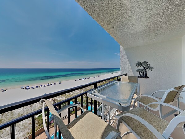 A balcony with a view of a beach, a palm tree decoration, and a table with chairs.