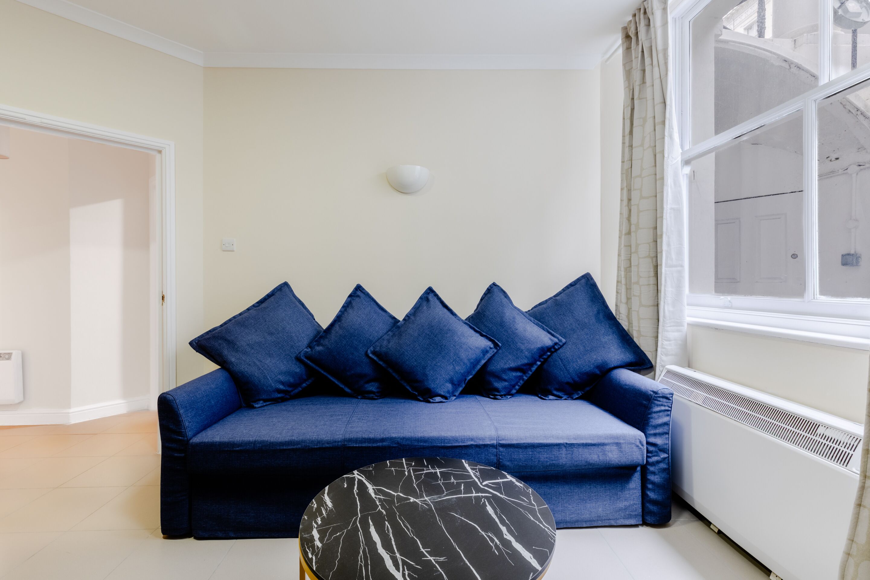 Ein Wohnzimmer mit einem blauen Sofa, einem runden Couchtisch und einem Fenster mit Vorhängen.