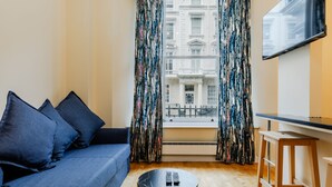 A modern living room with a blue sofa, a small round table, and a TV mounted on the wall. - Comfy Apartments in Queensway (London)