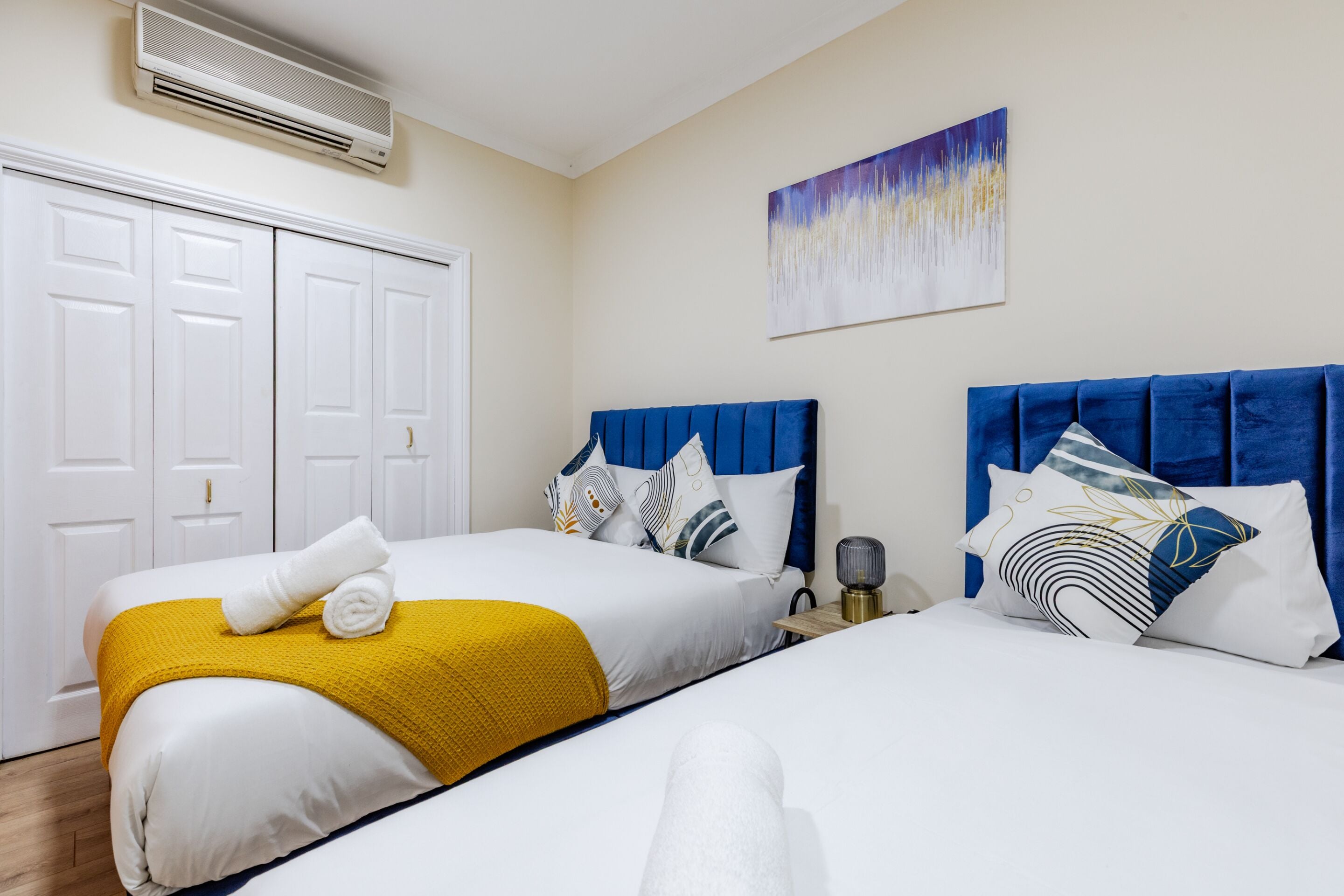 Habitación de hotel con dos camas, un armario blanco, un cuadro en la pared y un equipo de aire acondicionado.