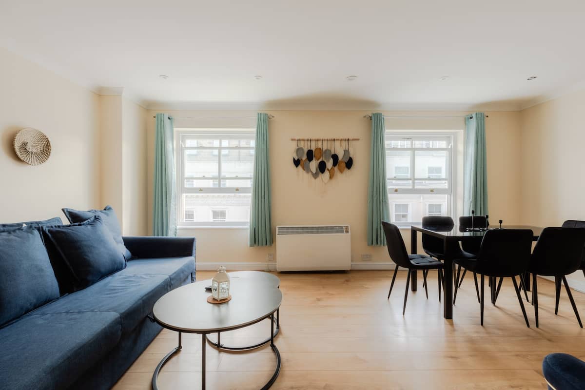 Ein modernes Wohnzimmer mit einem blauen Sofa, einem runden Couchtisch und einem Essbereich mit Tisch und Stühlen.