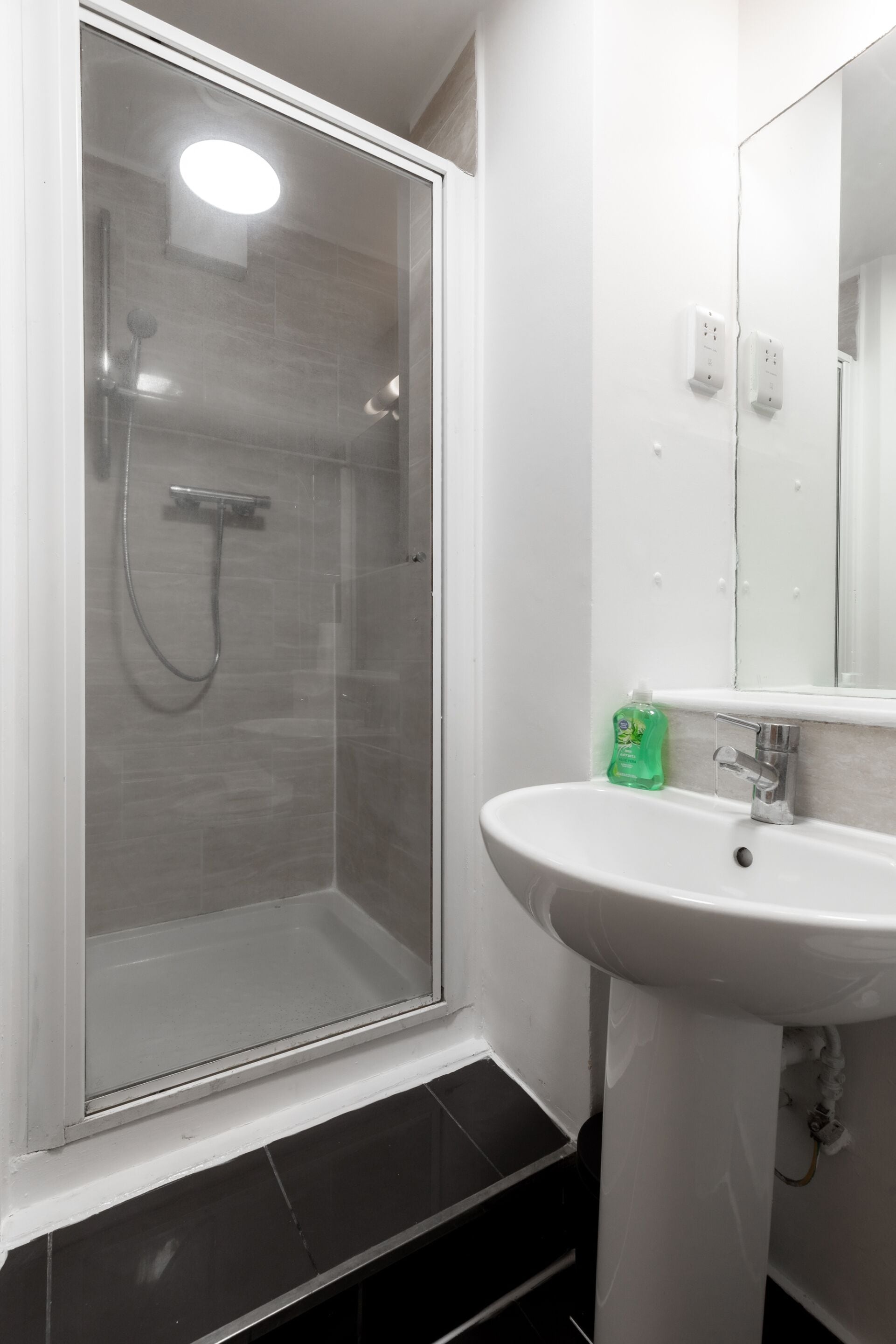 A bathroom with a glass-enclosed shower, a white sink, and a mirror.
