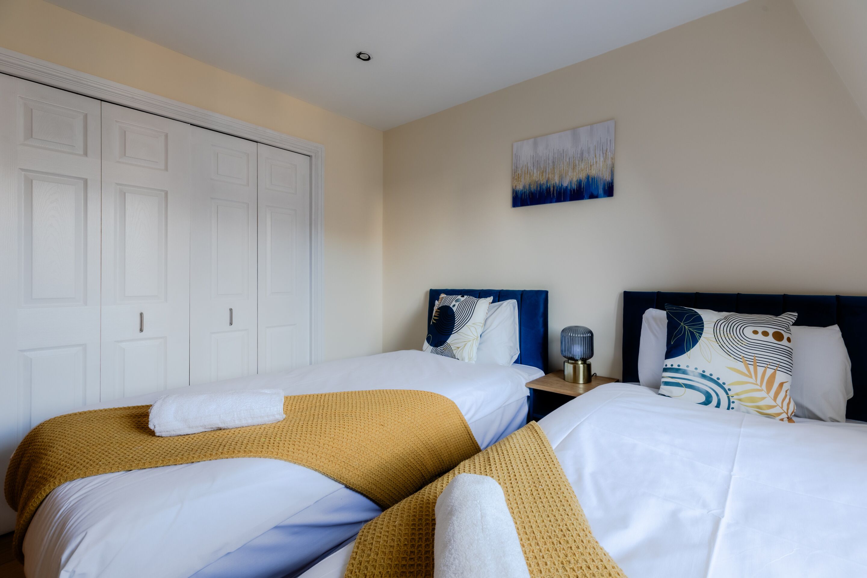 A hotel room with two beds, a white wardrobe, and a painting on the wall.