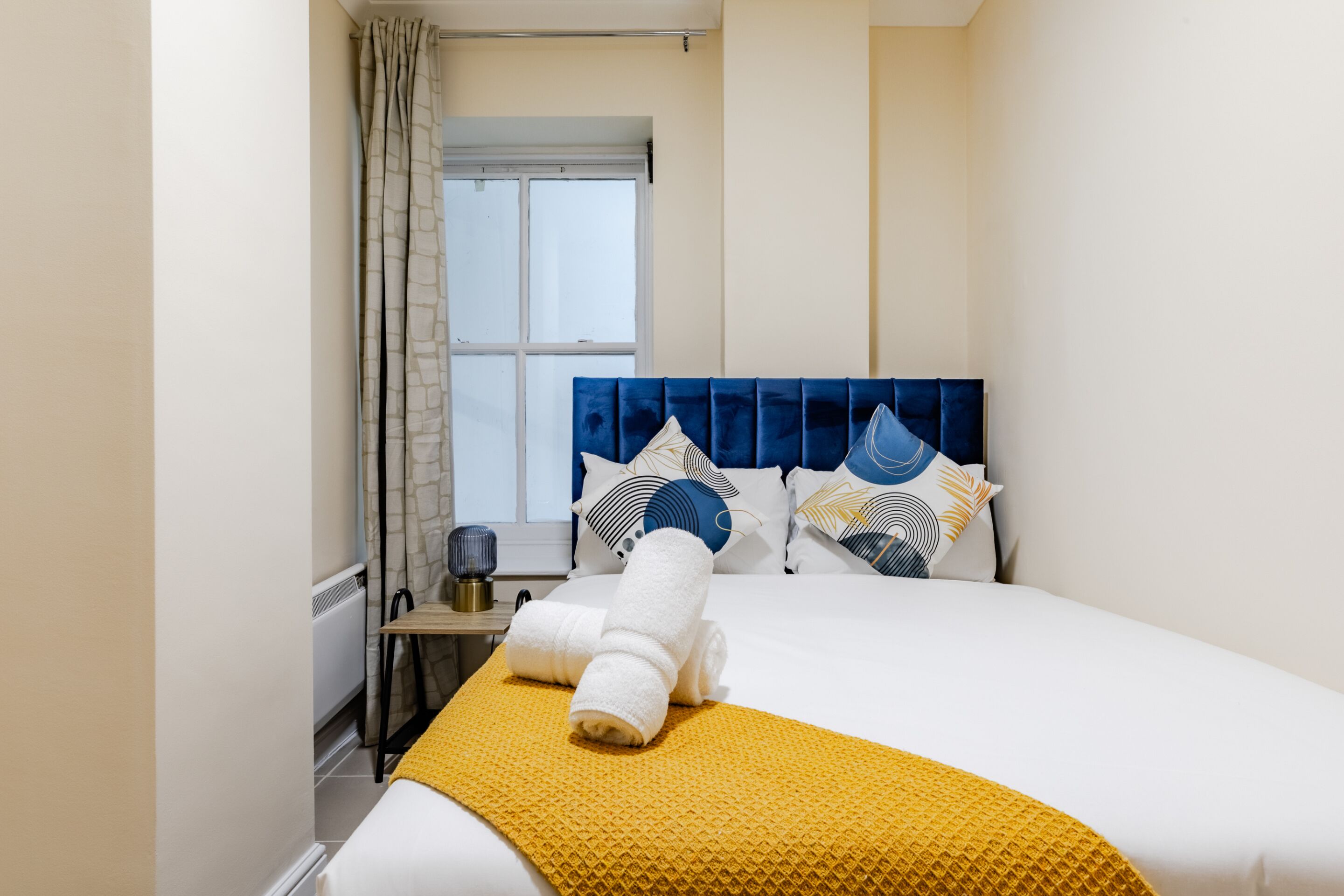 Habitación de hotel con cama, ventana, mesita de noche y una toalla sobre la cama.
