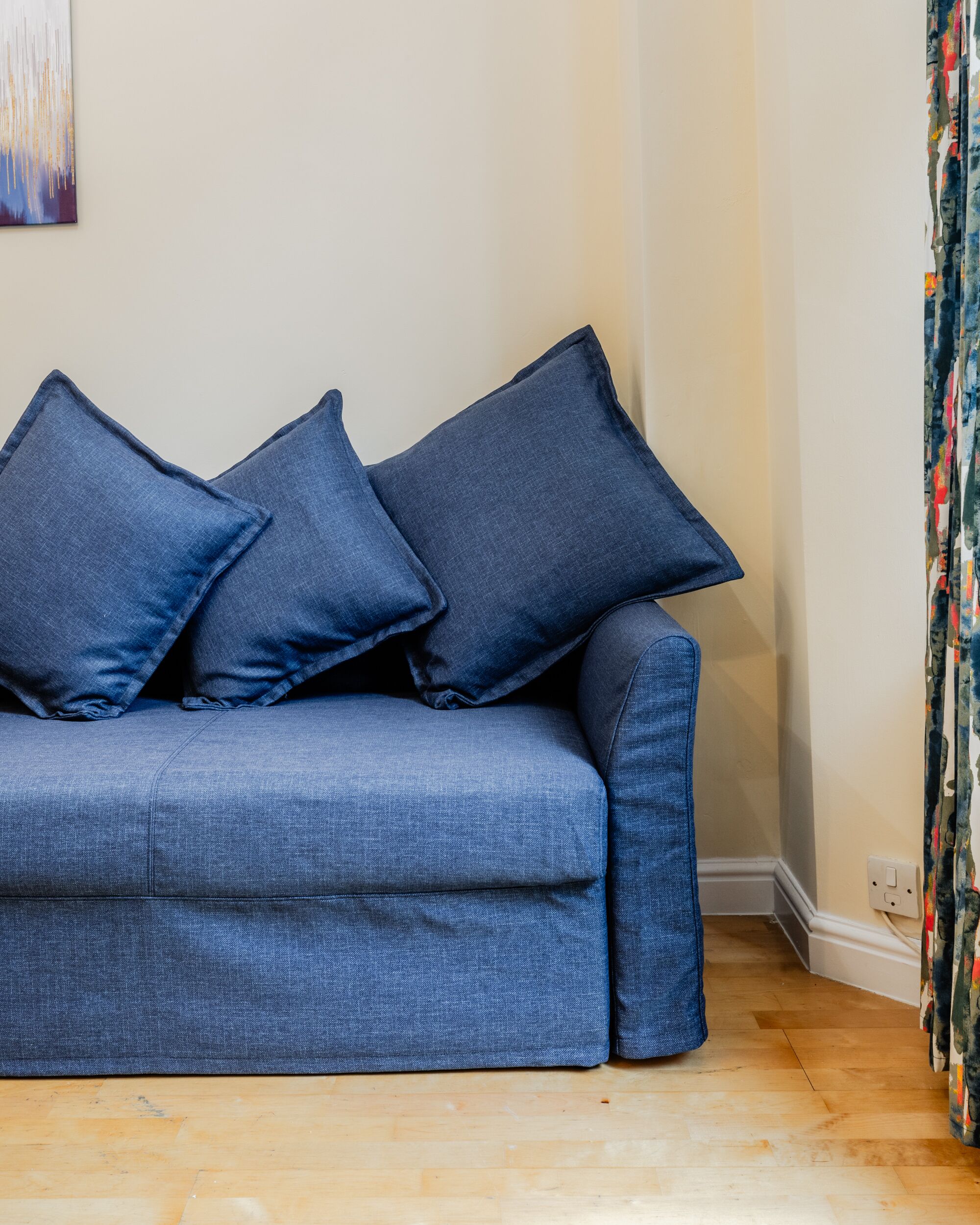 Un sofá azul con tres cojines en una habitación con suelo de madera y una pared lisa.