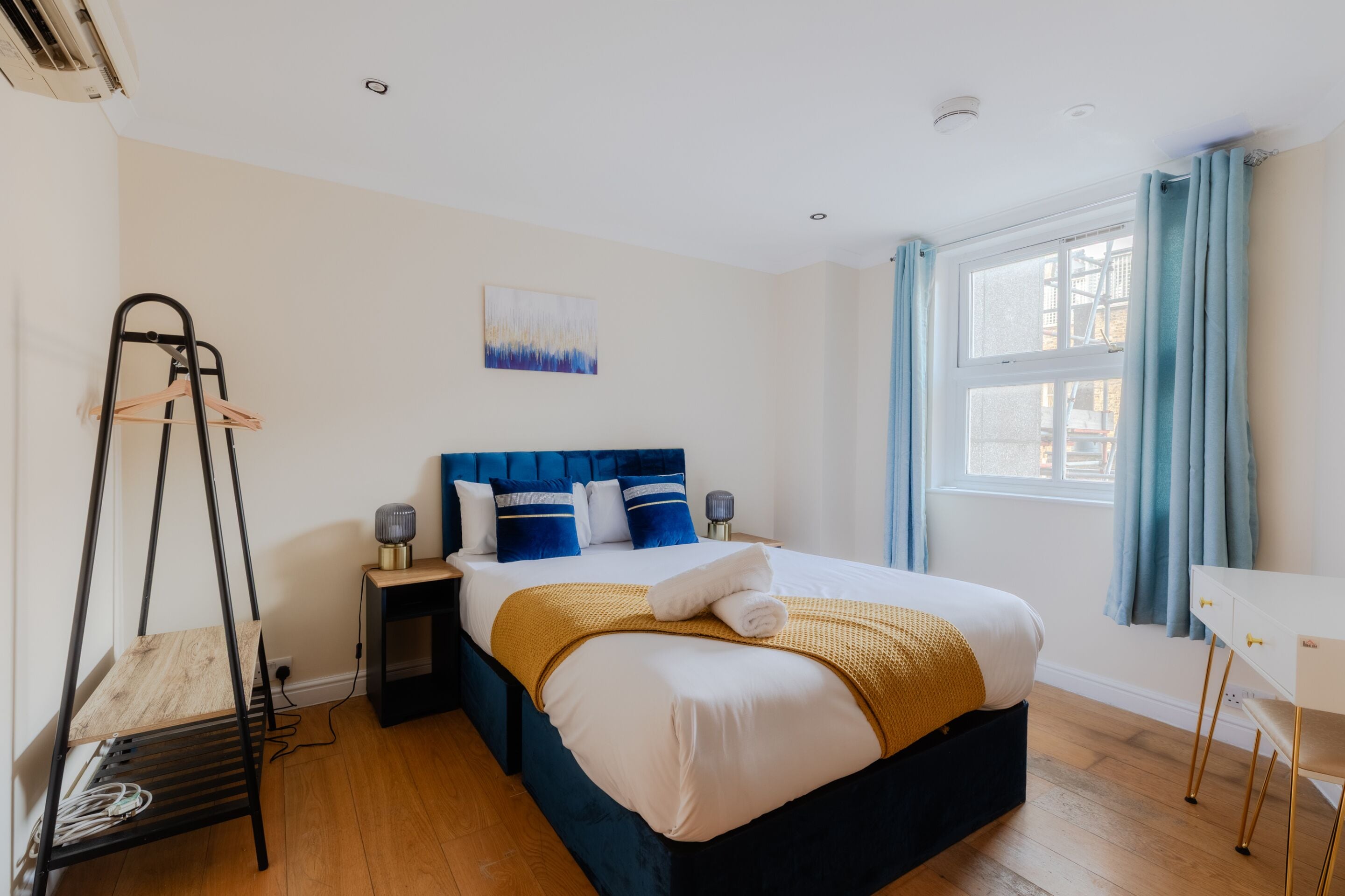 A bedroom with a bed, bedside tables, a hanging chair, a window with curtains, and a painting on the wall.