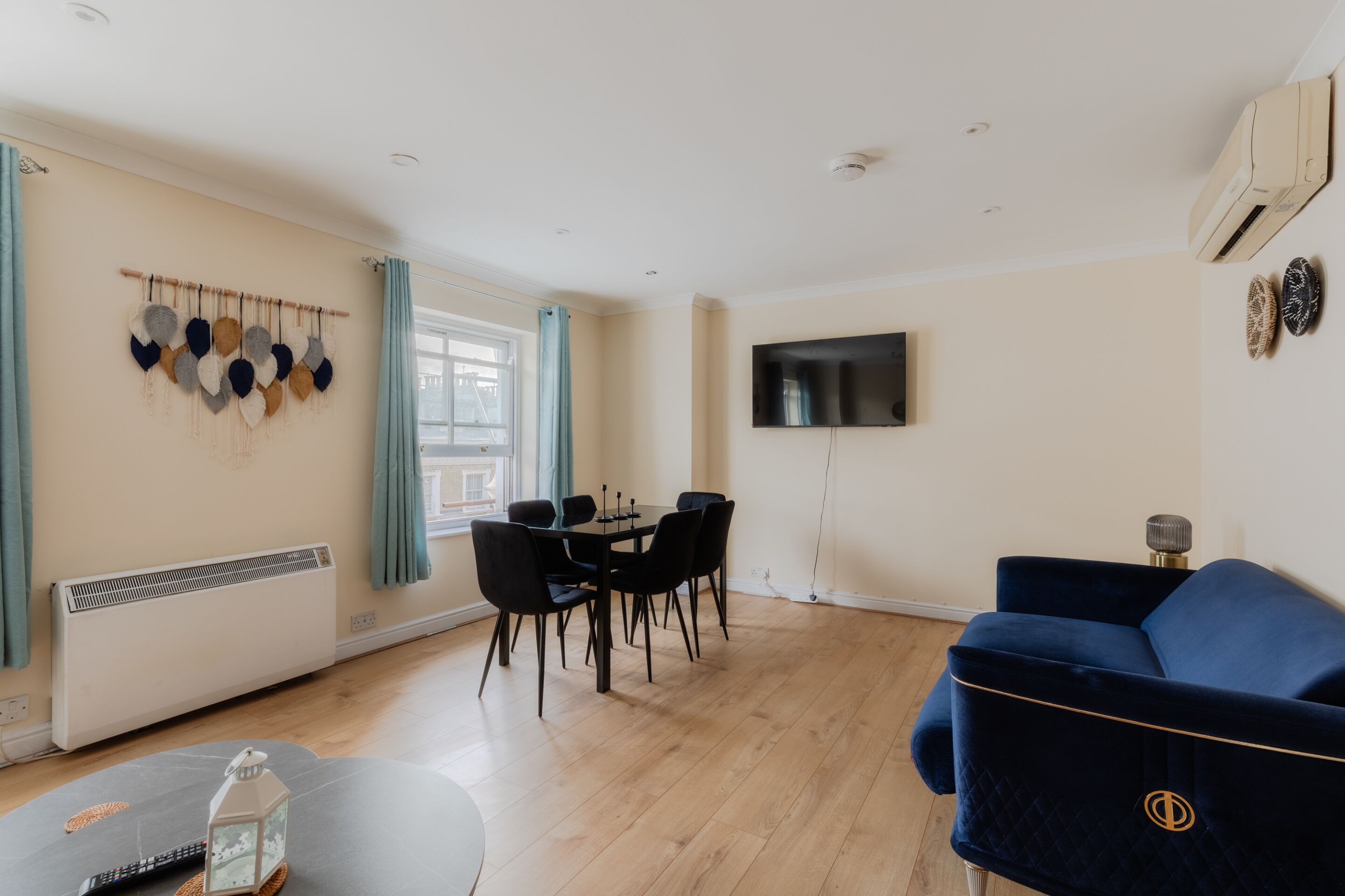 A living room with a dining area, a TV mounted on the wall, and a blue sofa.