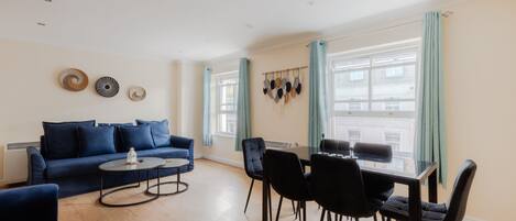 A modern living room with a blue sofa, a dining table with chairs, and a coffee table.