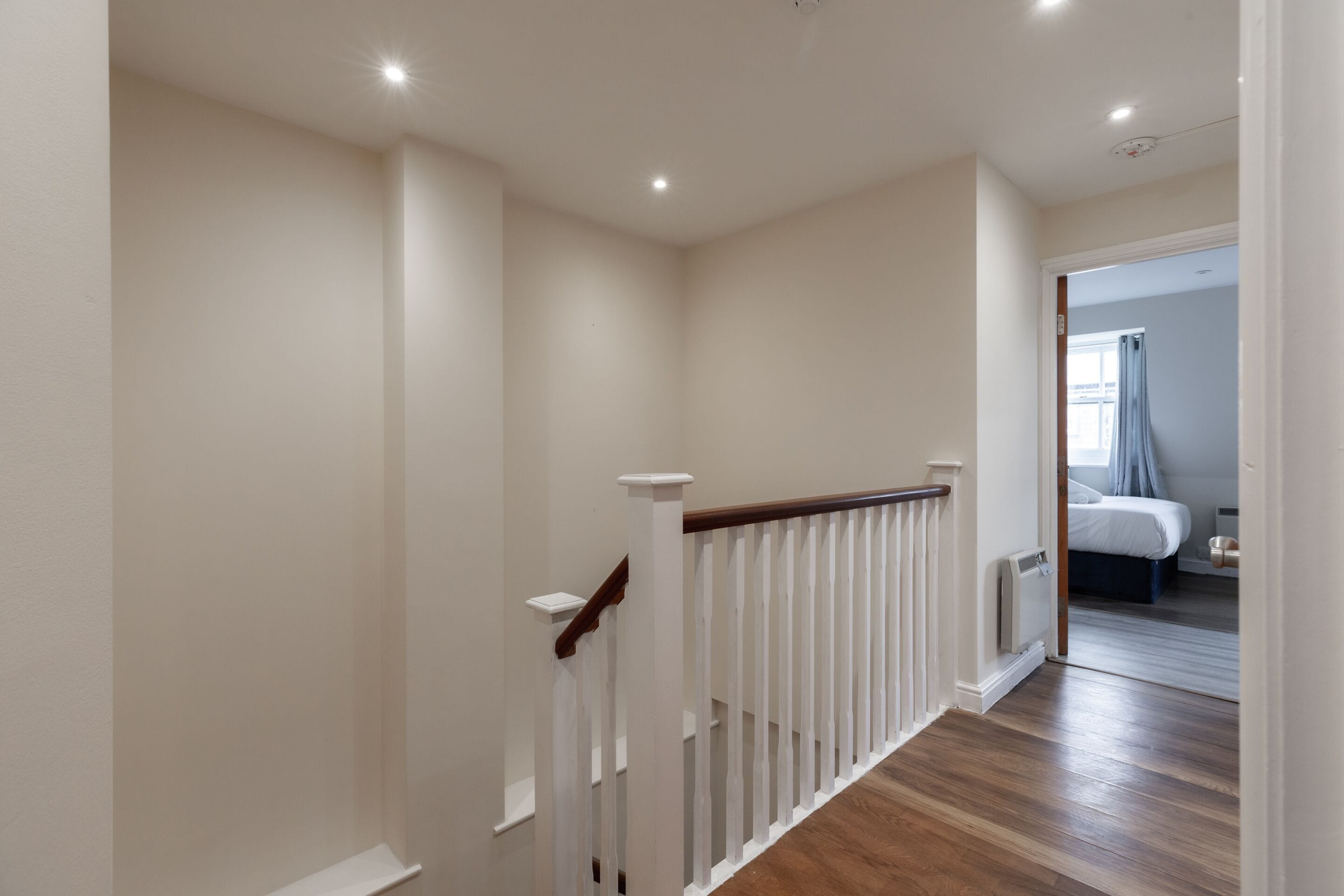 A hallway with a wooden floor, white walls, and a white railing.