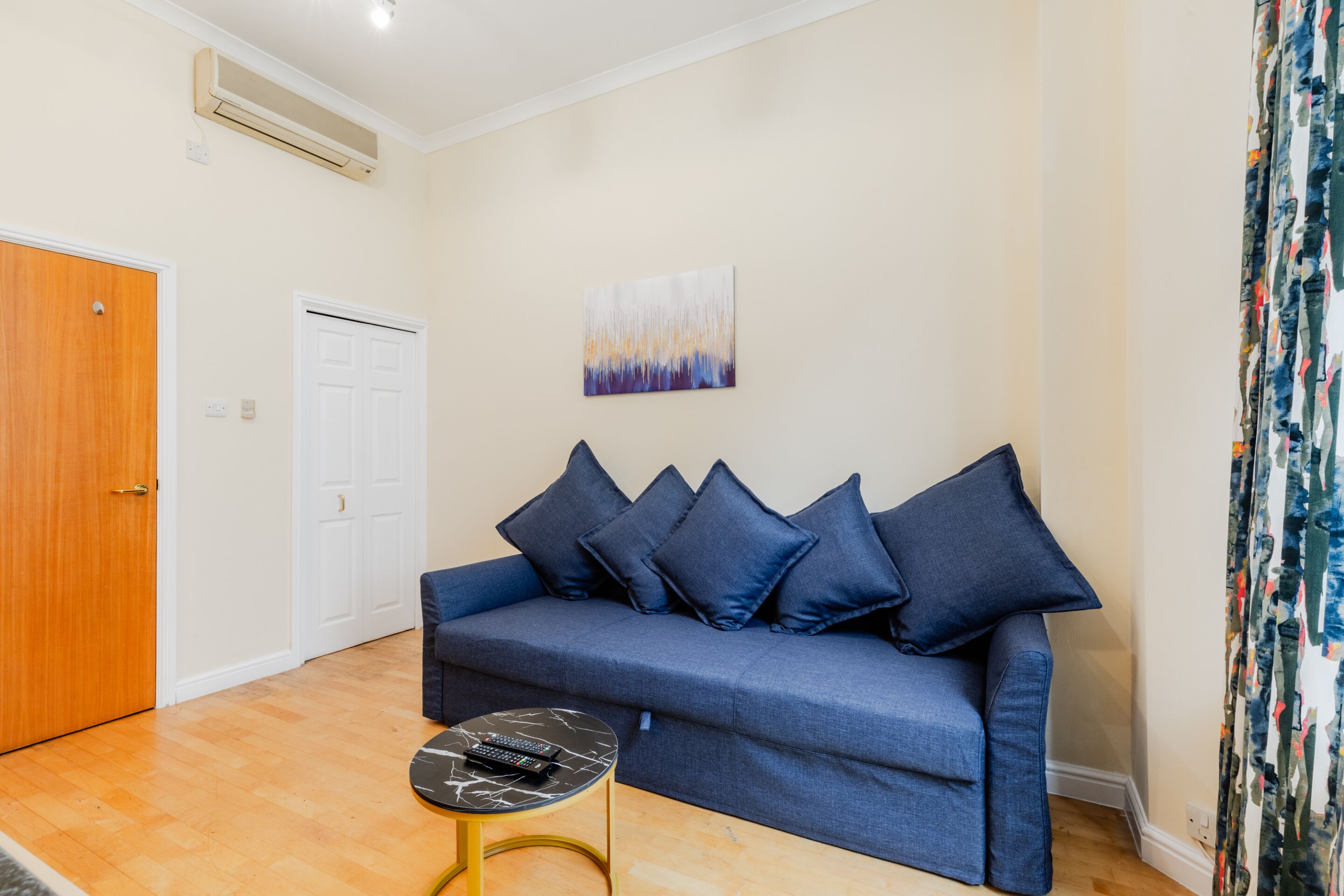 A living room with a blue sofa, a small round table, and a painting on the wall.