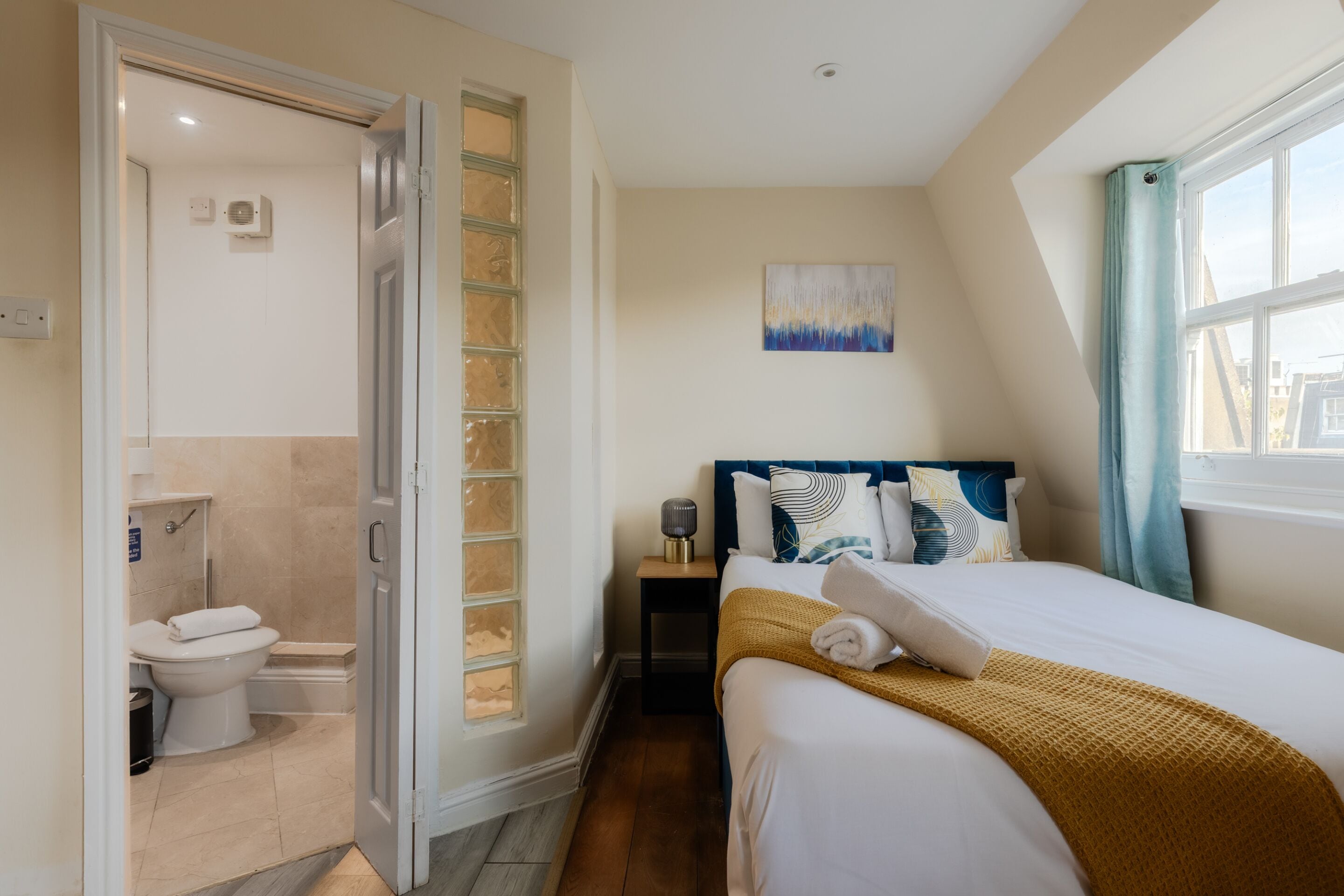 Ein Hotelzimmer mit Bett, Nachttisch, einem Gemälde und einem Badezimmer mit Toilette und Dusche.