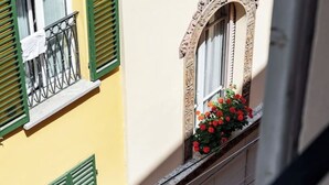 A building with a yellow facade, green shutters, and a window with red flowers. - Delightful House in the Center of Bologna Palazzo Storico (Bologna)
