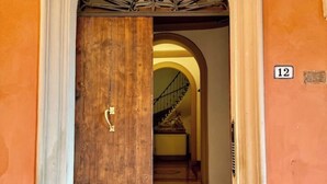 A wooden door with a brass handle, a number '12' sign on the wall, and a staircase leading to an upper floor. - Delightful House in the Center of Bologna Palazzo Storico (Bologna)