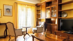 A living room with a wooden coffee table, two armchairs, a small round table, and a television. - Delightful House in the Center of Bologna Palazzo Storico (Bologna)