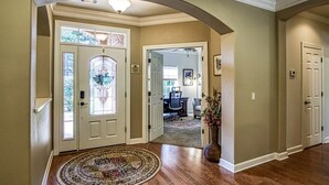 A hallway with a round carpet, a door with a stained glass window, and a vase with flowers.