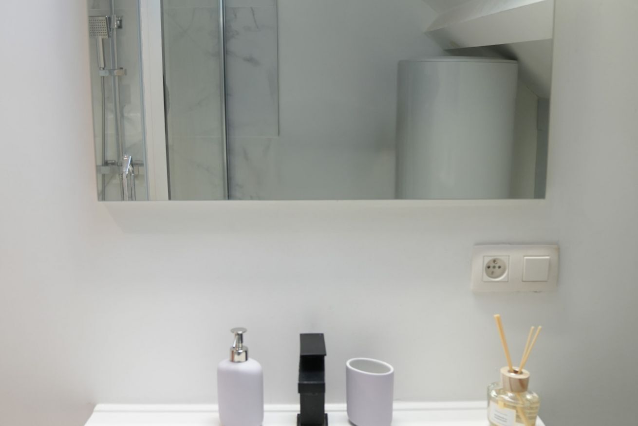 A bathroom with a mirror, a sink, a toilet, and a shower.