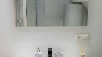 A bathroom with a mirror, a sink, a toilet, and a shower.