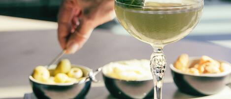 Un verre à cocktail agrémenté d’une garniture, un bol d’olives et un bol de gressins sur une table.