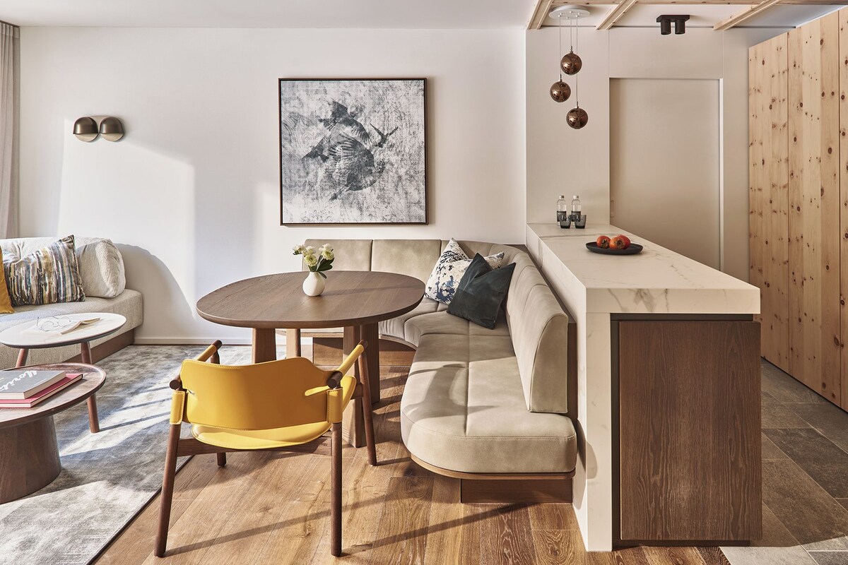 A modern living space with a round dining table, a sofa, a yellow chair, and a kitchen area with a marble countertop.