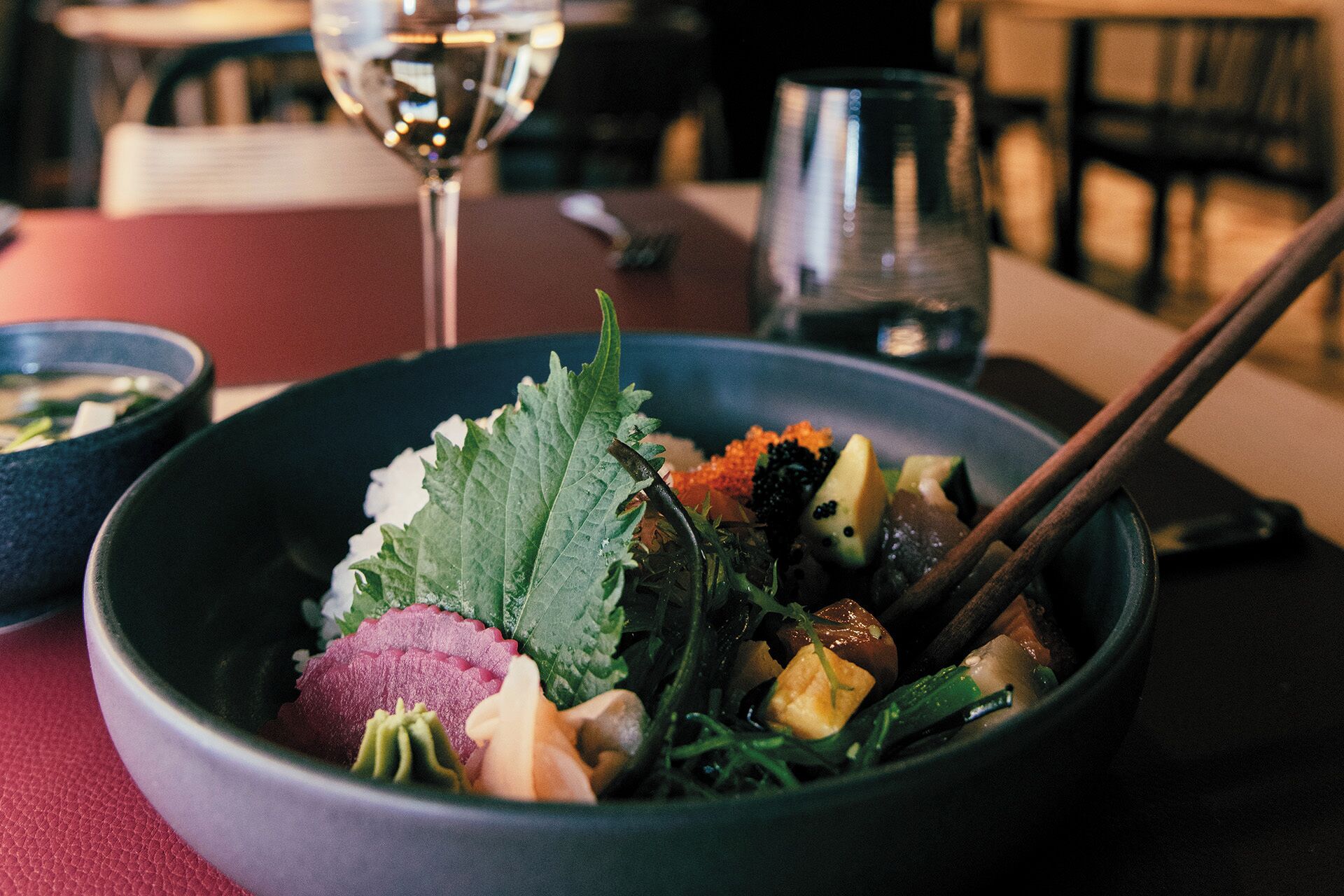 A bowl of food with chopsticks and a glass of water on a table.