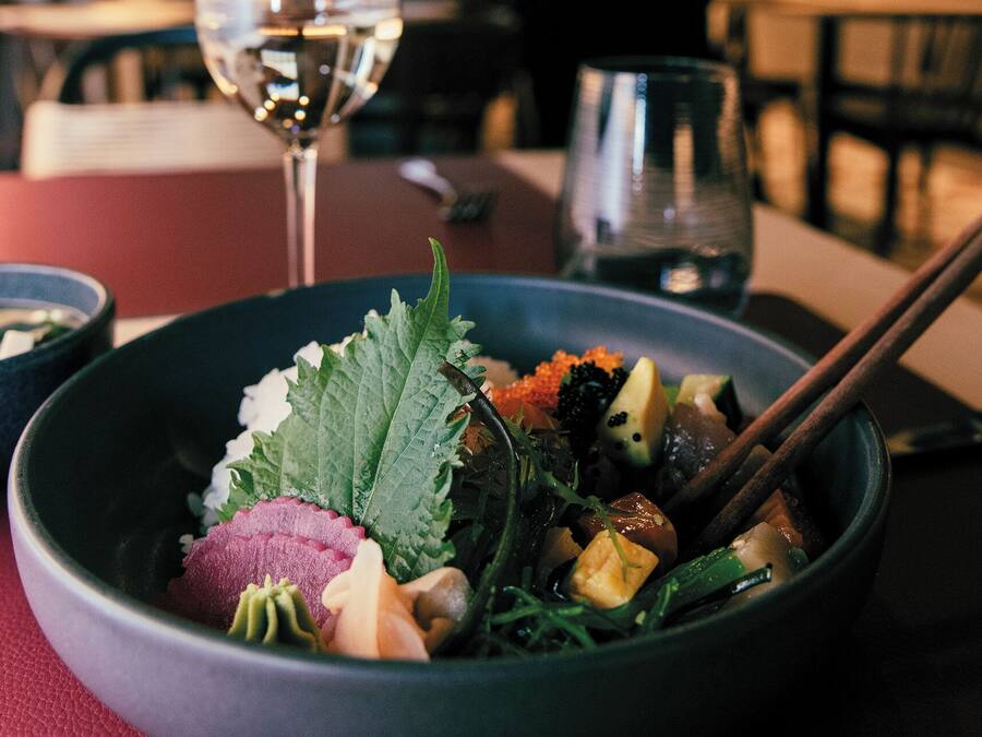 A bowl of food with chopsticks and a glass of water on a table.