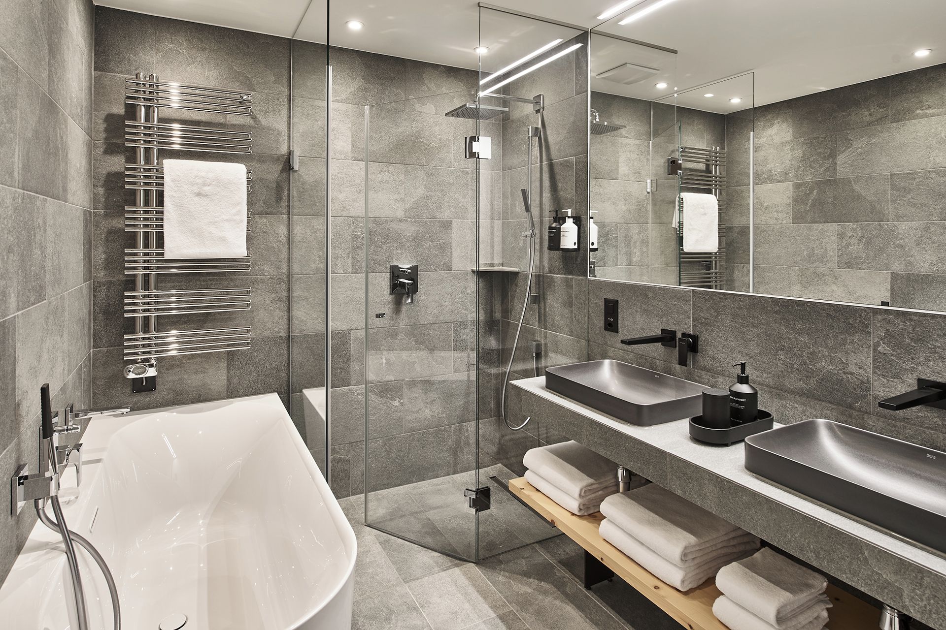 Un baño moderno con ducha envuelta en vidrio, una bañera independiente y dos lavamanos con toalleros.