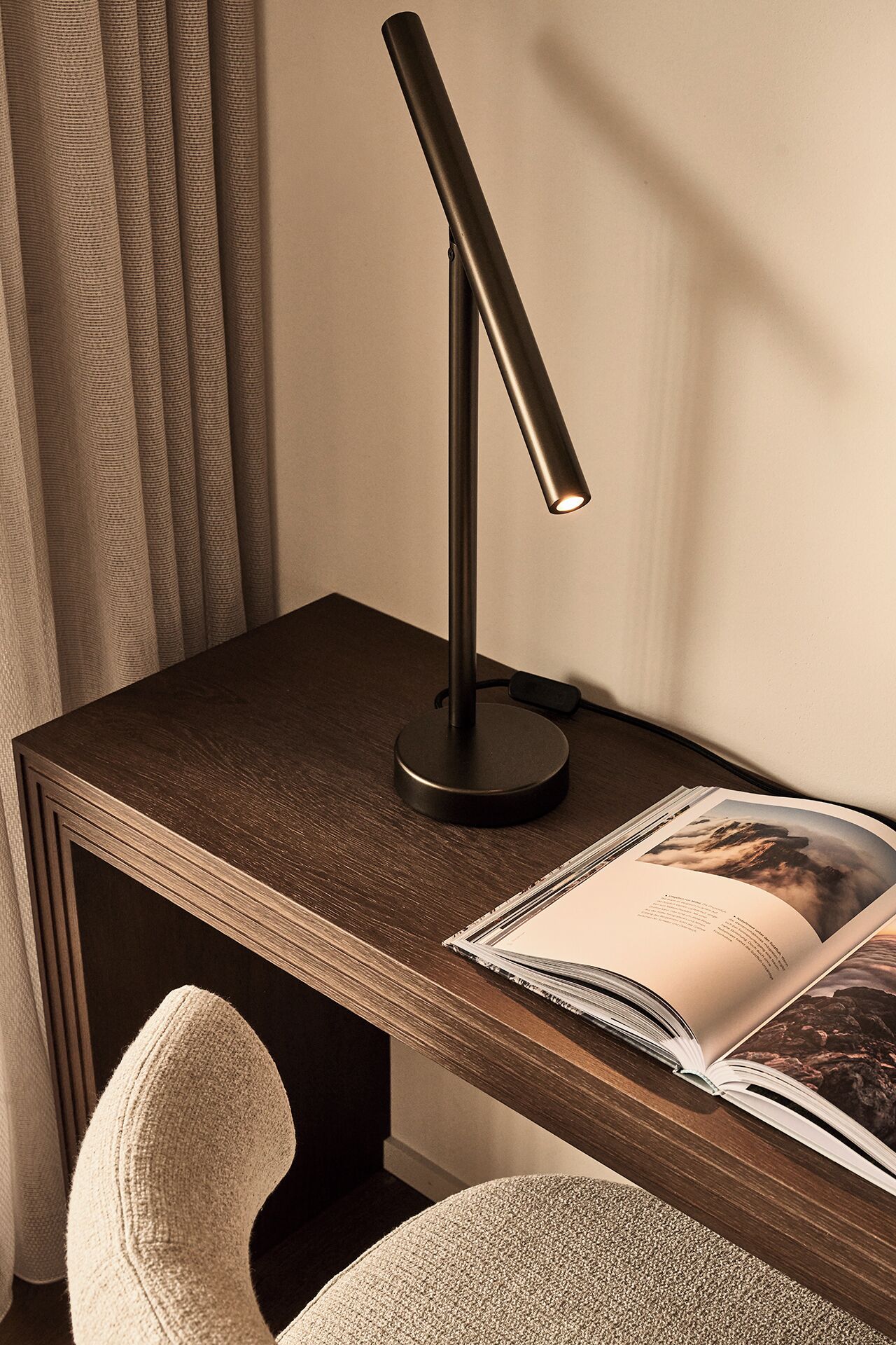 A desk with a modern desk lamp, a magazine, and a chair.