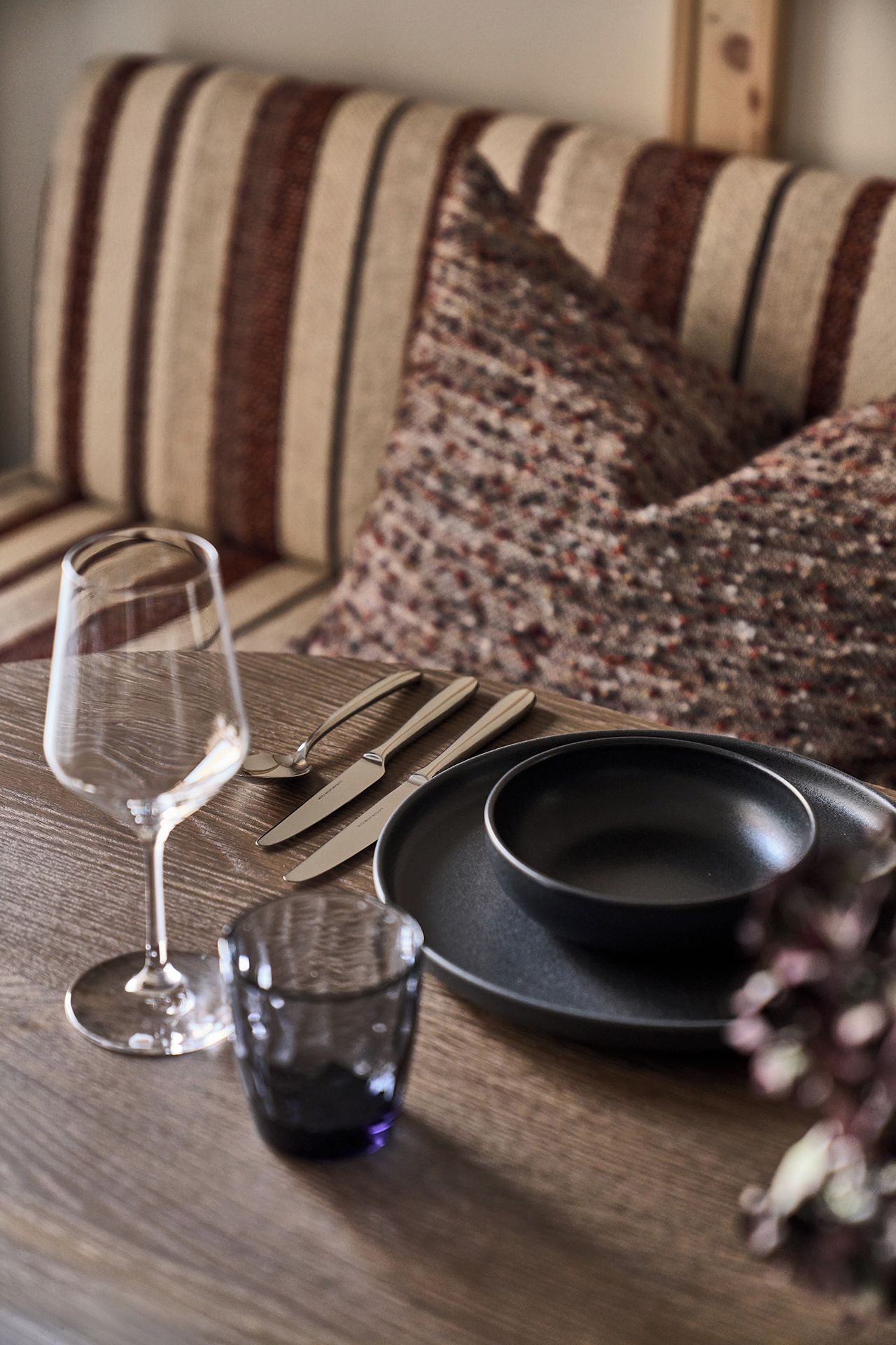 Una mesa de madera con un vaso de vino, cubiertos y platos.