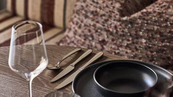 Una mesa de madera con un vaso de vino, cubiertos y platos.