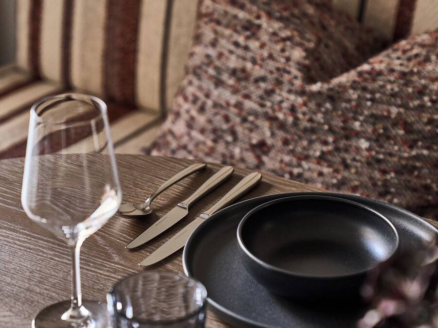 Una mesa de madera con un vaso de vino, cubiertos y platos.
