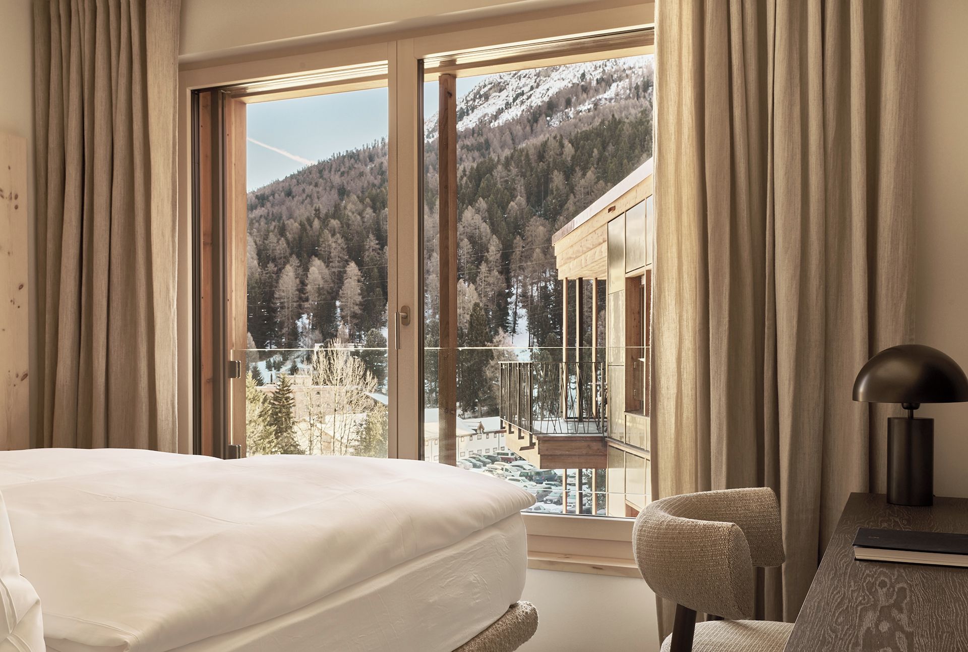 A hotel room with a large window offering a view of a snowy mountain and forest.
