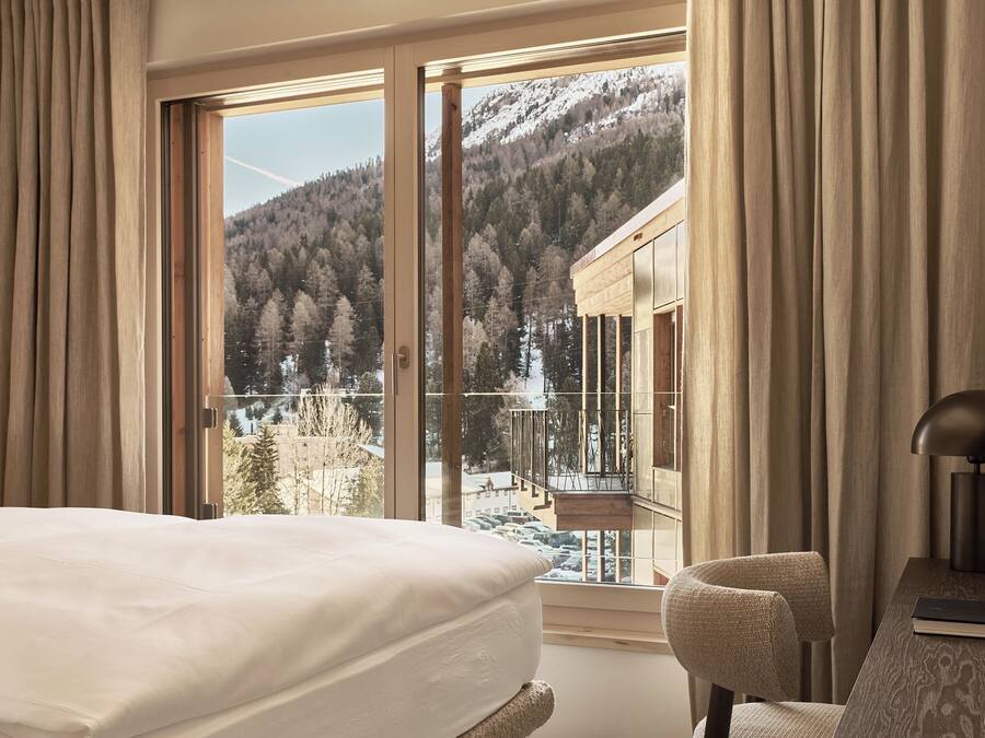 A hotel room with a large window offering a view of a snowy mountain and forest.