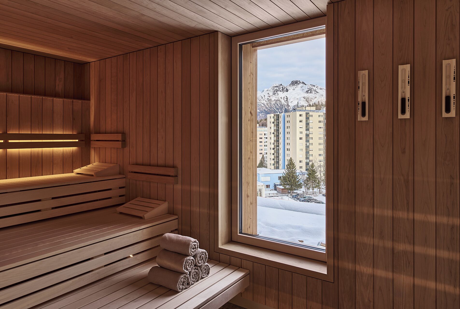 A sauna room with wooden benches and a large window overlooking a snowy landscape.