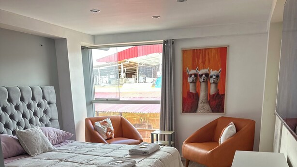 Quarto de hotel moderno com uma cama grande, duas poltronas, uma escrivaninha e um quadro de lhamas.