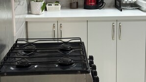 Uma cozinha com armários brancos, fogão a gás, cafeteira vermelha, uma planta e um porta-toalhas.