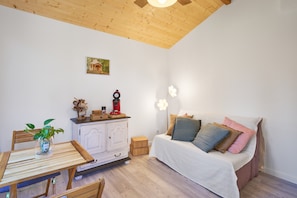 Una habitación con techo de madera, una cama con múltiples almohadas, un armario blanco, una pequeña mesa con una planta y una lámpara fijada a la pared.