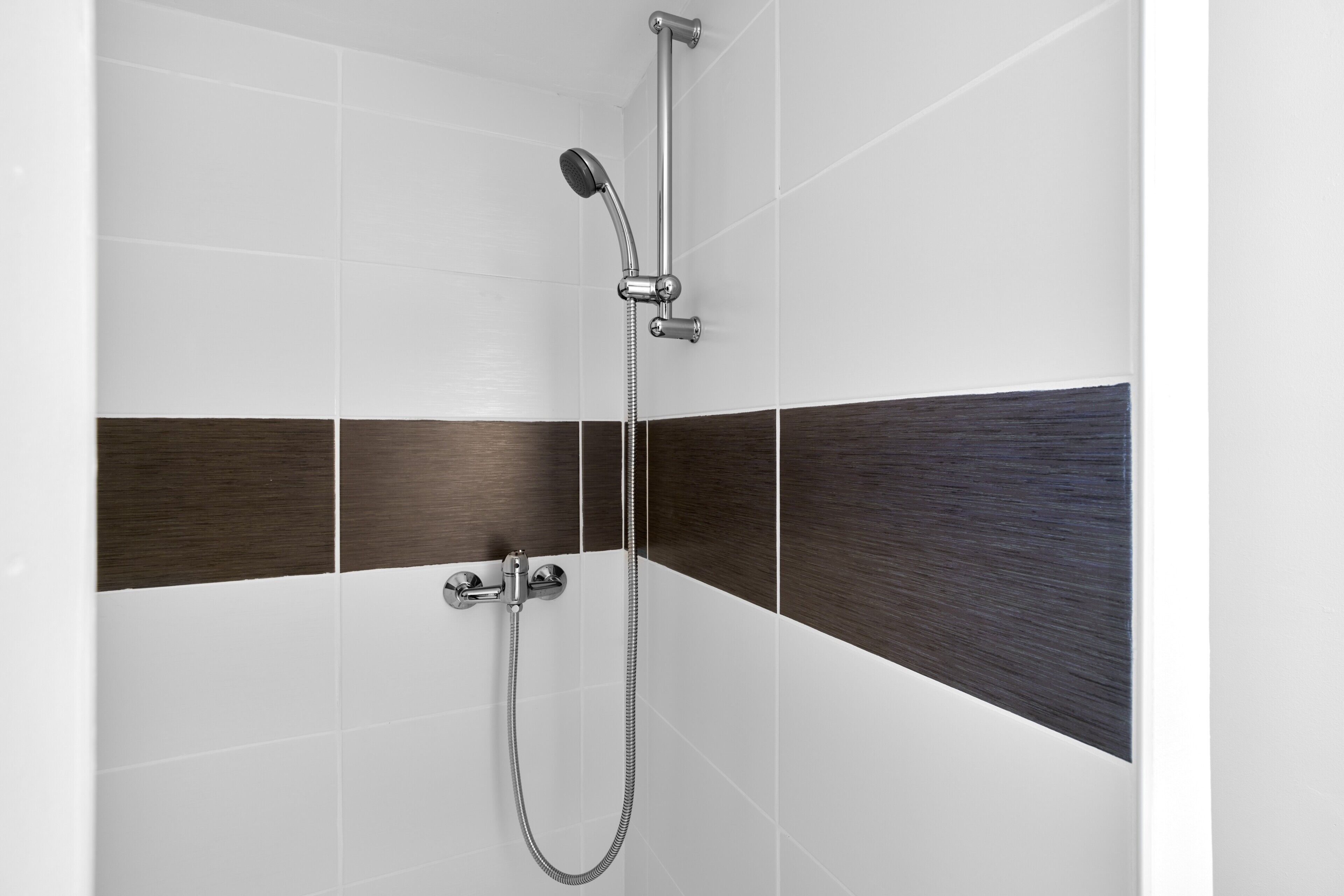 Une douche équipée d’un pommeau de douche à main et d’un robinet fixé au mur.