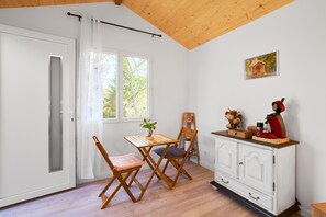 Una habitación con techo de madera, una puerta blanca, una mesa con sillas, un armario y una ventana con vista a árboles.