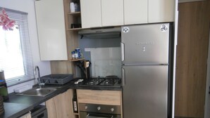 A compact kitchen with a stainless steel refrigerator, a built-in oven, a sink, and wooden cabinets. - Comfortable 3-bedroom mobile home near the beach (Saint-Brevin-les-Pins)