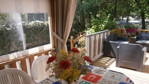 A covered outdoor seating area with a table set for two, featuring a nautical-themed tablecloth and a vase of flowers. - Comfortable 3-bedroom mobile home near the beach (Saint-Brevin-les-Pins)