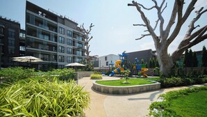 Un terrain de jeux équipé de toboggans et de structures d’escalade, entouré d’un jardin aménagé et bordé d’un bâtiment doté de balcons.