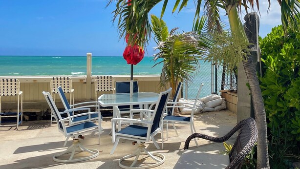 Een terras met een tafel en stoelen, een palmboom en uitzicht op de oceaan.