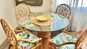 Een ronde glazen tafel met een gevlochten onderstel, omringd door vier rieten stoelen met bloemenmotieven.