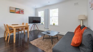 Una sala de estar moderna con una mesa de comedor de madera, una mesa baja negra, un sofá gris y un televisor sobre un mueble.