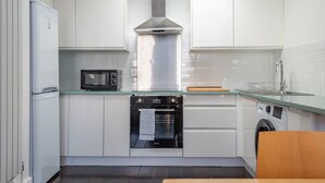 Una cocina moderna con armarios blancos, una campana extractora de acero inoxidable, un microondas, un horno y una lavadora.